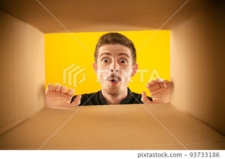 Wow. Surprised man unpacking, opening carton box and looking inside with wide open eyes. Delivery, surprise, gift, wow emotions concept. 93733186