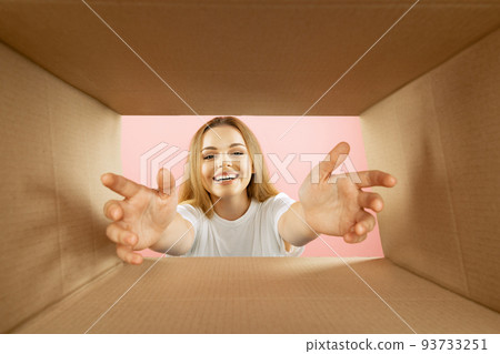 Beautiful young exressive girl opening, unpacking carton box and looking inside. Emotions, black friday, holidays, online shopping concept 93733251