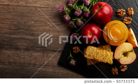 Mason jar with honey, honeycomb, red apples and walnuts on kitchen table 93733373