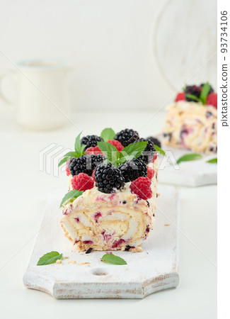 Baked meringue roll with cream and fresh fruits on a white wooden board, delicious dessert 93734106