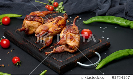 Frying carcasses of quails lie on a wooden board with vegetables, a black table 93734107