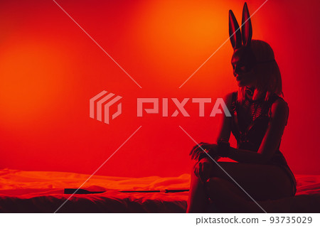 submissive sexy girl in underwear and a bunny mask sitting on the bed puts handcuffs on hands in bedroom 93735029