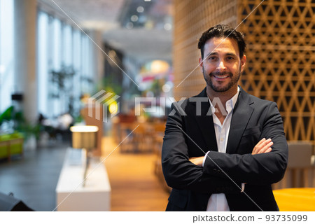 Portrait of happy handsome Hispanic businessman at coffee shop with arms crossed 93735099