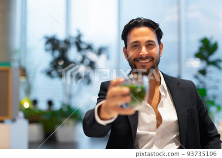 Portrait of happy handsome Hispanic businessman at coffee shop having green tea Portrait of happy handsome Hispanic businessman at coffee shop having green tea 93735106