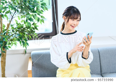 Young woman in plain clothes, living room, smartphone 93735990