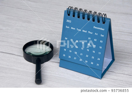 December 2022 blue color desk calendar on wooden desk with copy space and magnifying glass. 93736855