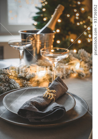 Christmas festive table setting with garland, champagne, stylish gray plate with napkin ring. Close up. Christmas festive table setting with garland, champagne, stylish gray plate with napkin ring. Close up. 93736952