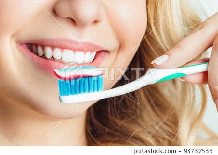 Close-up of woman brushing teeth. The girl holds a toothbrush and smiles. 93737533