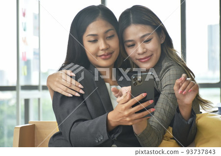 happy two busimess Asian woman looking at mobile phone for relaxing after work in office happy two busimess Asian woman looking at mobile phone for relaxing after work in office 93737843
