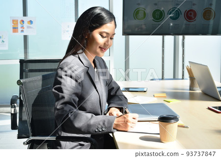 Asian woman holding pen writing on note book with laptop background in office meeting room Asian woman holding pen writing on note book with laptop background in office meeting room 93737847