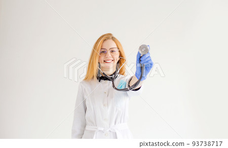 a doctor girl with red hair holds a stethoscope in her hands on a white isolated background. a doctor girl with red hair holds a stethoscope in her hands on a white isolated background. 93738717