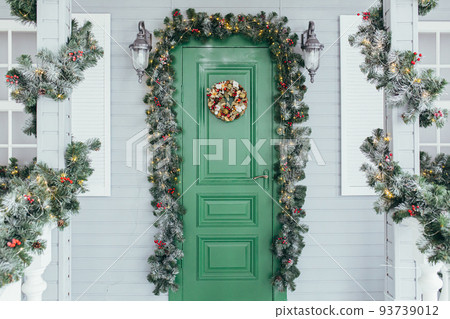 Green door entrance to the house. Christmas festive deco decorated with Christmas tree branches Green door entrance to the house. Christmas festive deco decorated with Christmas tree branches 93739012
