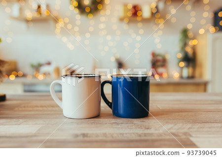 close-up photo of two Christmas cups, on New Year's background, Christmas tree and colorful lights, in the kitchen on the table 93739045