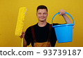 A young man in uniform holds a bucket of water and a mop in his hands. Janitor cleans and disinfects the space 93739187