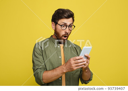 Shocked man in glasses checking newest mobile app or online offer, looking at smartphone screen in excitement Shocked man in glasses checking newest mobile app or online offer, looking at smartphone screen in excitement 93739407