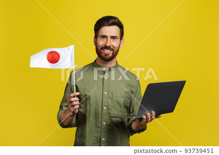 Happy man holding Japan flag and laptop computer, standing over yellow studio background 93739451