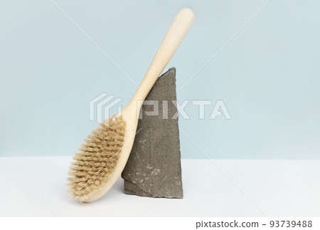 Natural wooden body brush balancing on rocks, on light-blue background. Massage, relax, spa. Zero waste product. Natural wooden body brush balancing on rocks, on light-blue background. Massage, relax, spa. Zero waste product. 93739488
