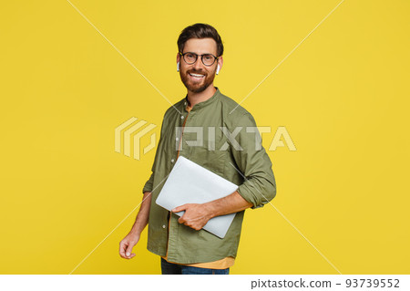 Happy middle aged male freelancer posing with laptop over yellow studio background, looking and smiling at camera Happy middle aged male freelancer posing with laptop over yellow studio background, looking and smiling at camera 93739552