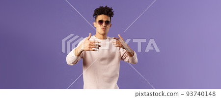 Portrait of sassy and carefree young hipster guy with dreads, wearing sunglasses dancing and gesturing while singing during rap battle, dance hip-hop on party, standing purple background 93740148