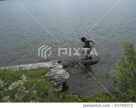Man fisherman angler on lake shore fly fishing and caught trout or char fish in Gieddavrre lake in Sweden Lapland on Padjelantaleden hiking trail. 93740553