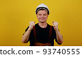 A young caucasian guy wearing a hard hat and builder clothes over isolated yellow background prays with his hands with a hopeful expression on his face and then rejoices in success 93740555