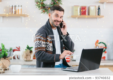 Happy and successful freelance entrepreneur working on laptop at home talking on the phone during the New Year holidays completes the project by deadline Happy and successful freelance entrepreneur working on laptop at home talking on the phone during the New Year holidays completes the project by deadline 93740832