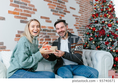 Young family together celebrate New Year and Christmas, couple man and woman give gifts to each other sitting on sofa at home happy and in love 93740871