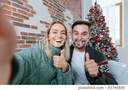Woman and man at home looking at smartphone camera greet friends with holidays, young family during New Year holidays and Christmas Woman and man at home looking at smartphone camera greet friends with holidays, young family during New Year holidays and Christmas 93740880