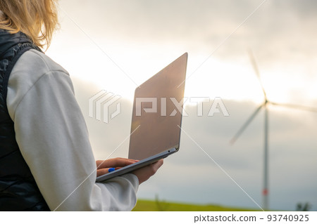 Female engineer checking the stability work of windmill with laptop in the field at sunlight. Green energy of future 93740925