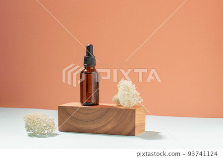 Bottle with pipette made of dark glass, cosmetic product woodenpedestal. Pastel coral background Bottle with pipette made of dark glass, cosmetic product woodenpedestal. Pastel coral background 93741124