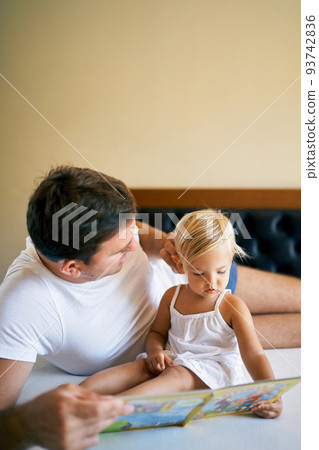 Dad straightens hair of little daughter reading a book 93742836