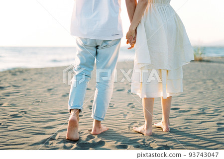 Man and woman stand on the sand barefoot holding hands. Cropped Man and woman stand on the sand barefoot holding hands. Cropped 93743047