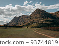 Trail and fences leading into a mountain with a blue cloudy sky. 93744819