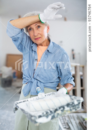 Portrait of an elderly tired female house painter in renovated room Portrait of an elderly tired female house painter in renovated room 93746764