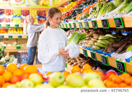 Smiling teen girl choosing fresh romaine lettuce in fruit and vegetable store 93746765
