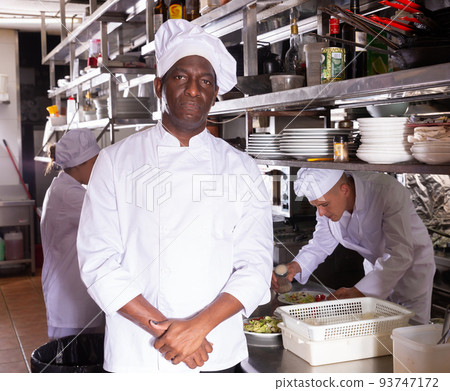 Experienced African American chef of restaurant posing in kitchen Experienced African American chef of restaurant posing in kitchen 93747172
