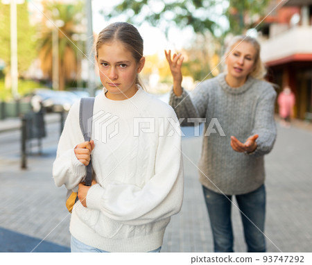 Frowning teenage girl listening to reprimanding from mother oncity street Frowning teenage girl listening to reprimanding from mother oncity street 93747292