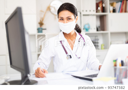 Kazhahstani female doctor in medical mask is working behind laptop 93747382