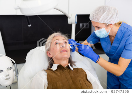 Qualified cosmetologist giving beauty injections to elderly female client Qualified cosmetologist giving beauty injections to elderly female client 93747396