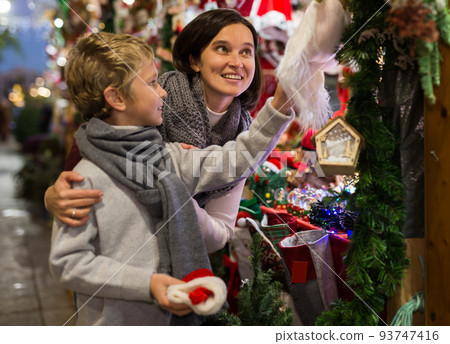 Tween boy with mother looking for Christmas decorations on street market Tween boy with mother looking for Christmas decorations on street market 93747416