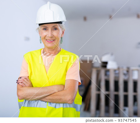 Portrait of positive builder woman in protective helmet and yellow vest in renovated room Portrait of positive builder woman in protective helmet and yellow vest in renovated room 93747545