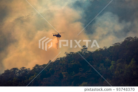 Fire fighting helicopter dropping water onto wildfire 93748370