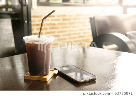 Iced black coffee with straw in plastic cup on table. 93750071