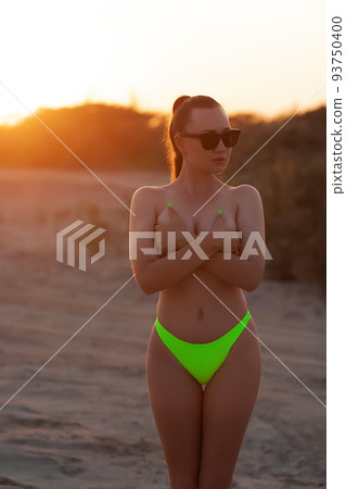 Fit sexy lady in bikini covering breast on sandy seashore at sundown Fit sexy lady in bikini covering breast on sandy seashore at sundown 93750400