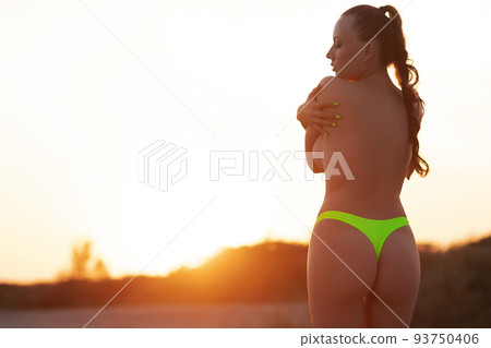 Sensual woman in bikini standing on sandy beach and covering breast at sunset Sensual woman in bikini standing on sandy beach and covering breast at sunset 93750406