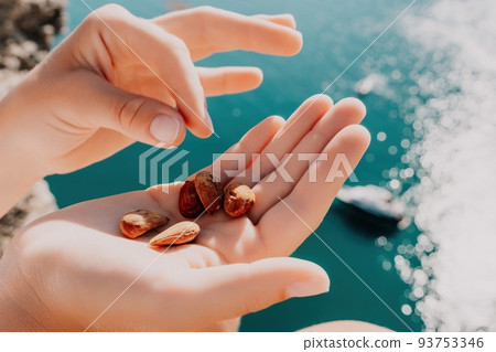 Young milky almond nuts in womans hand. A young caucasian woman eating fresh almond after morning fitness yoga near sea. Only hands are visibly. Healthy vegan food. Young milky almond nuts in womans hand. A young caucasian woman eating fresh almond after morning fitness yoga near sea. Only hands are visibly. Healthy vegan food. 93753346