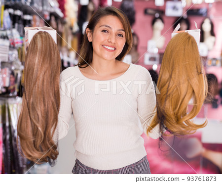 Smiling girl choosing wigs from natural hair in store 93761873
