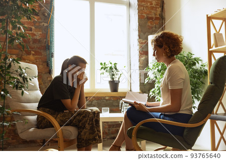Sad young man in military uniform at therapy session with female psychiatrist, indoors. Concept of mental health, post-traumatic syndrome, help and support Sad young man in military uniform at therapy session with female psychiatrist, indoors. Concept of mental health, post-traumatic syndrome, help and support 93765640