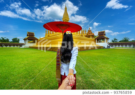 Women tourists holding man's hand and leading him to Phra that luang in Vientiane, Laos. 93765859