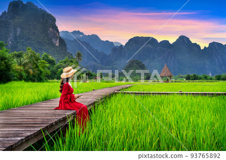 Young woman sitting on wooden path with green rice field in Vang Vieng, Laos. 93765892